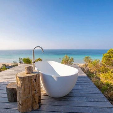 Outdoor bathtub with ocean view on wooden deck.