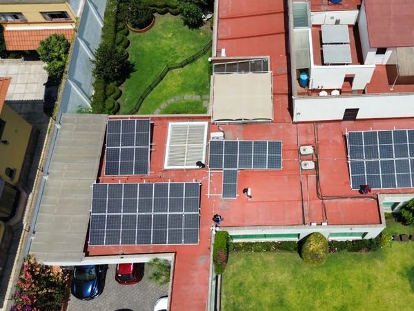 Solar panels installed on a red rooftop with adjacent green garden areas.