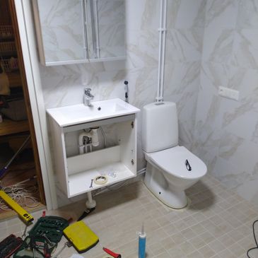 Bathroom under renovation with open sink cabinet and tools.