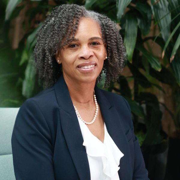 Professional woman with gray curly hair wearing a navy blazer and pearl necklace.
