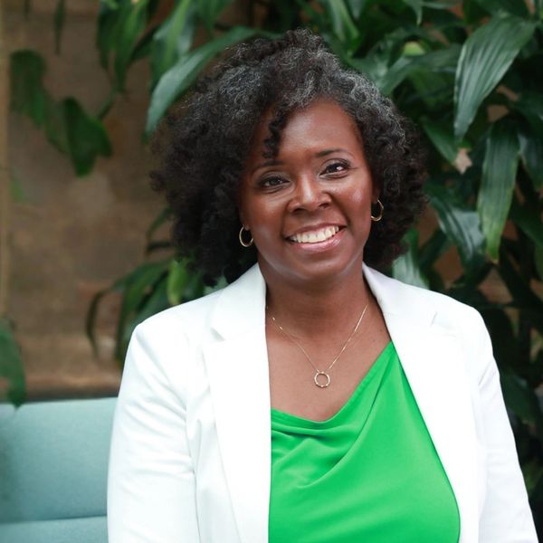 Smiling woman with curly hair wearing a green top and white blazer.