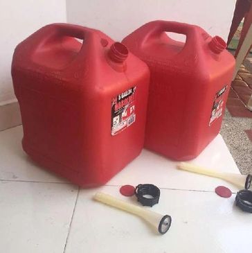 Two red 5-gallon gasoline containers with removable spouts and caps on a tiled floor.