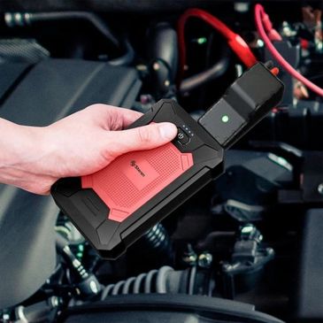 Hand holding a portable jump starter near a car engine.