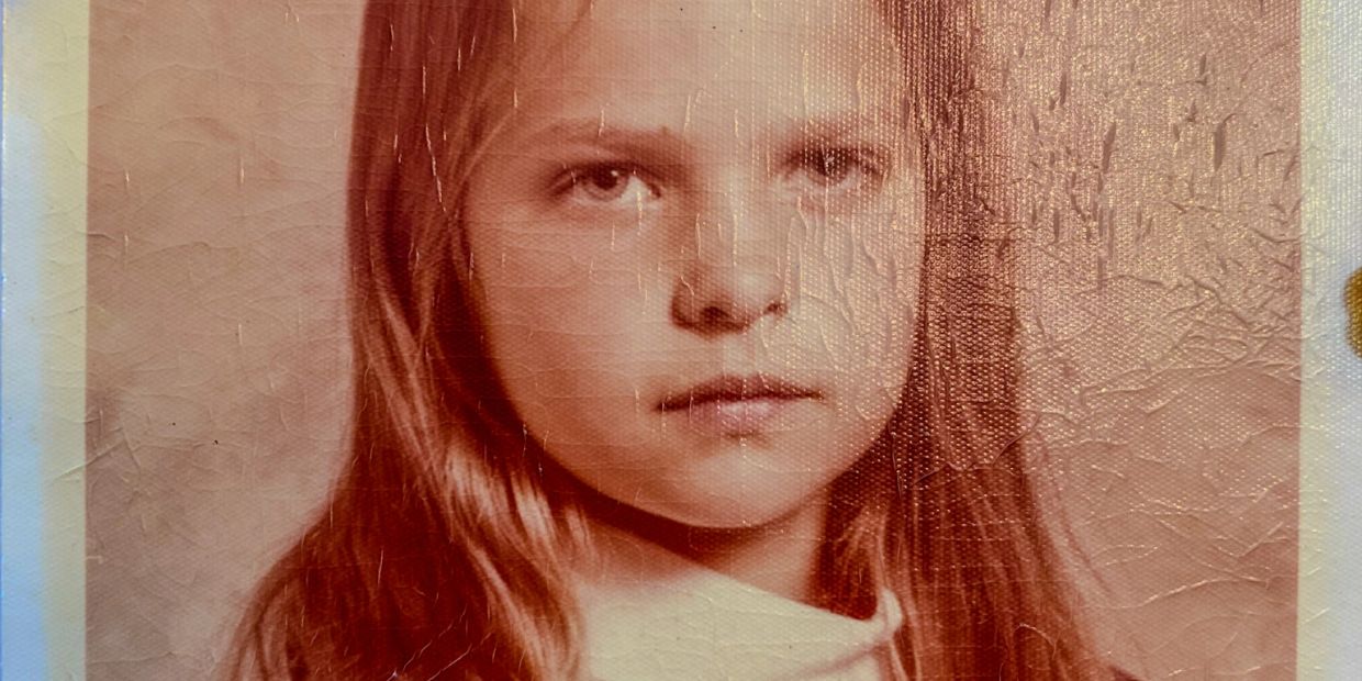 Close-up of a young girl with long hair in a vintage photo showing texture and wear.