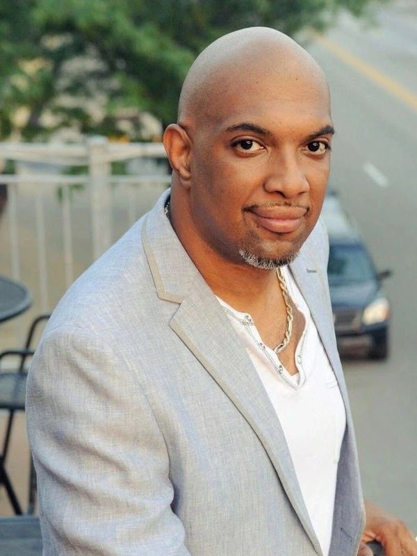 Confident man in light gray blazer smiling outdoors.
