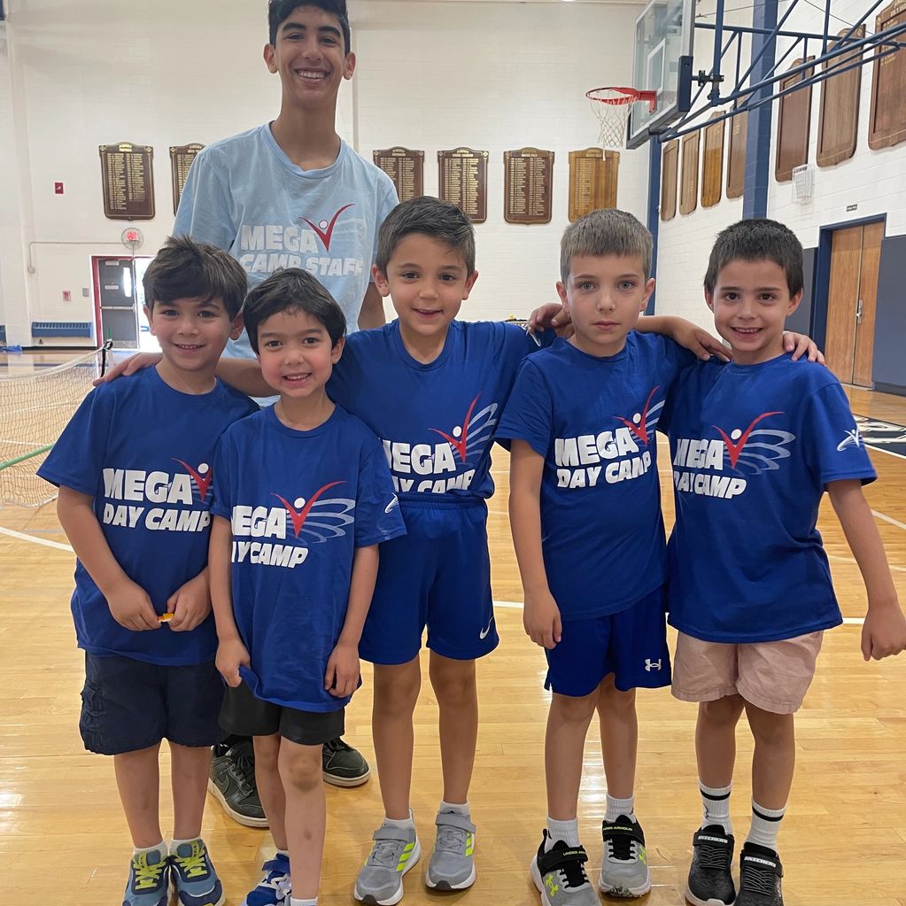 A group of boys and a camp counselor posing in a gym with Mega Day Camp shirts.