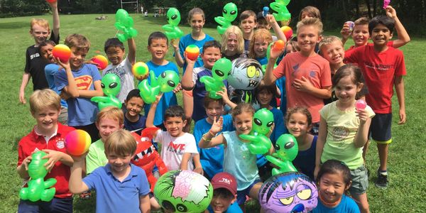 A joyful group of children holding inflatable aliens and colorful balls outdoors.