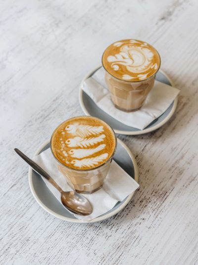 Two lattes with intricate latte art on white napkins and plates.