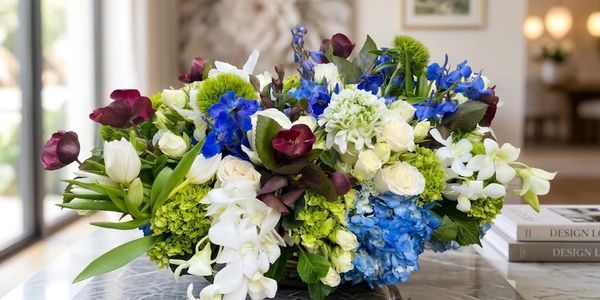 Custom floral arrangement with blue hydrangeas, white blooms, burgundy flowers, and fresh green acce