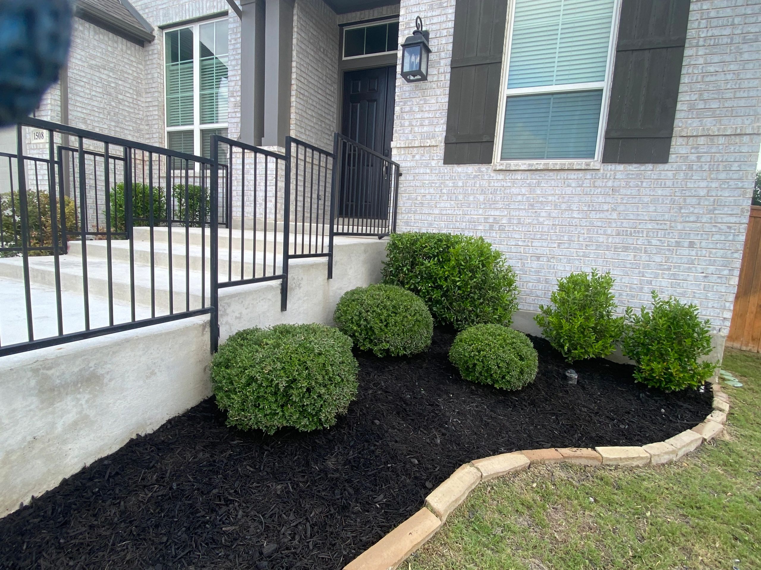 Neatly mulched front yard with trimmed bushes and stone border.