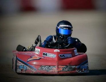 A go-kart racer in a red kart on a dirt track.