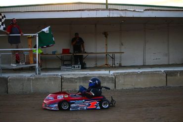 A go-kart racer crossing the finish line with a green flag waved.