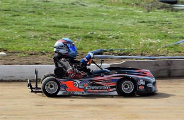 A racer in a helmet driving a go-kart on a dirt track.