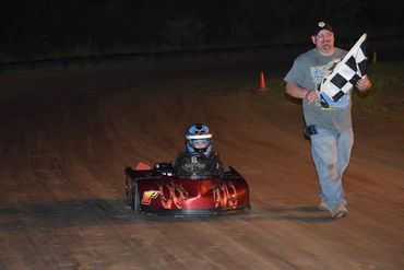 A child in a go-kart finishes a race as a man holds a checkered flag.
