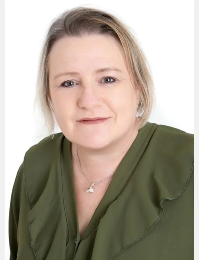 Portrait of a woman wearing an olive green blouse and a pendant necklace.