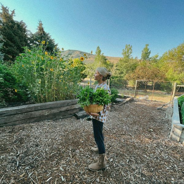 A woman holding a basket of greenery in a garden during daylight.