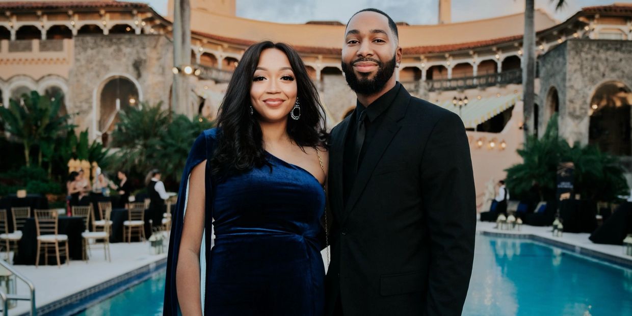 A couple dressed elegantly by a pool at a luxurious outdoor venue.