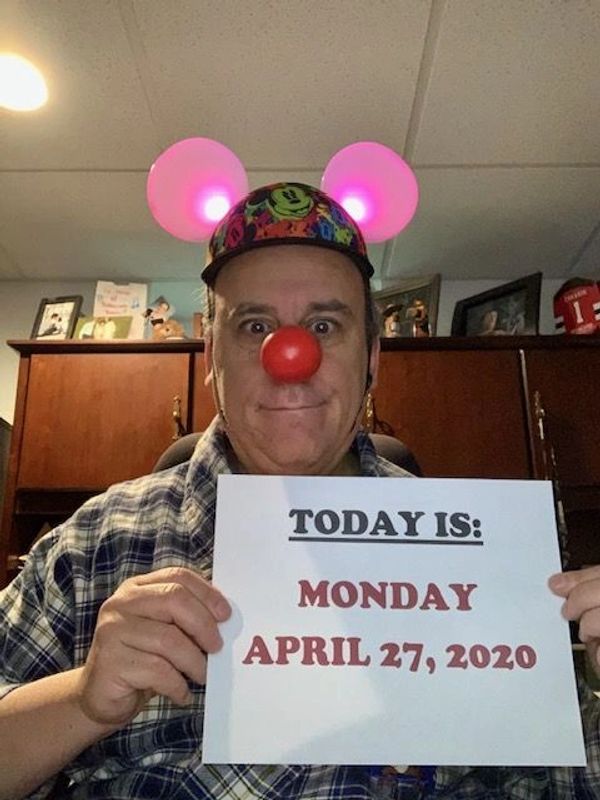 Man wearing light-up Mickey ears and red clown nose holds date sign.