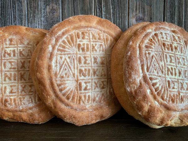 Three round breads with religious inscriptions on a wooden surface.