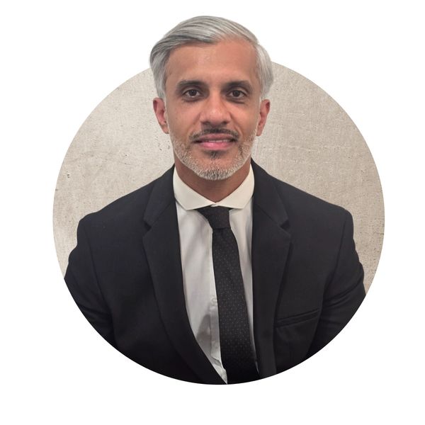 Professional man in a black suit and tie against a neutral background.