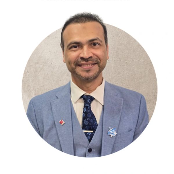 Smiling man in a blue suit and tie against a neutral background.