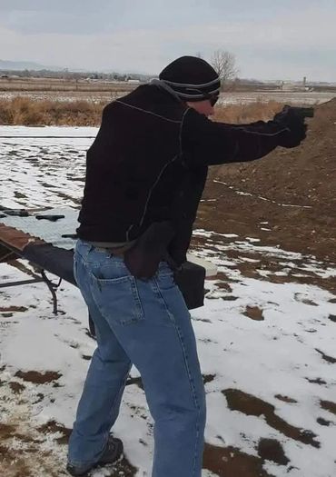 Man in winter clothes aiming a handgun outdoors in snow-covered area.
