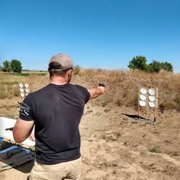 Man aiming a handgun at targets on a sunny outdoor shooting range.