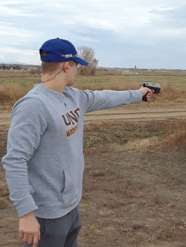 Person aiming a handgun outdoors in a field.