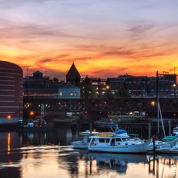 Boats docked by the harbor at sunset with city buildings in the background.