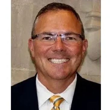 Smiling man wearing glasses and a suit with a yellow striped tie.