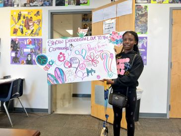 Young girl holding a colorful peace poster in a classroom.