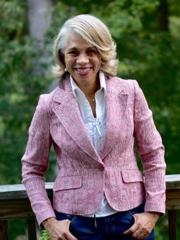 Smiling woman in a pink textured blazer outdoors.