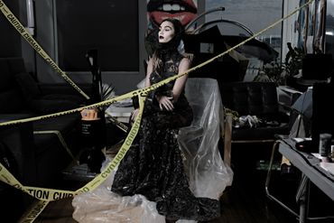 Woman in elegant black dress surrounded by caution tape in a cluttered room.