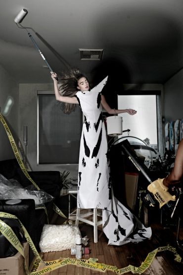 Woman in a black-and-white dress painting a ceiling, surrounded by caution tape and tools.