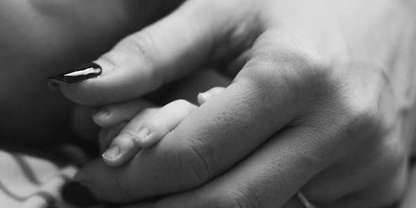 Black and white photo of an adult hand holding a baby's hand gently.