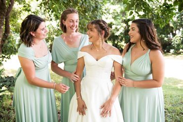 Bride smiles with her laughing bridesmaids in a bright glade.