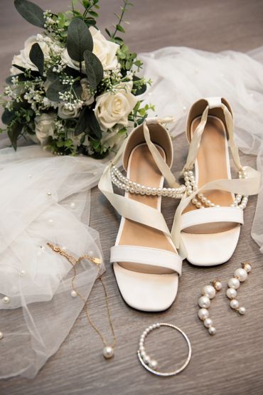 A collection of the brides accessories for her wedding with her shoes and pearls all around.