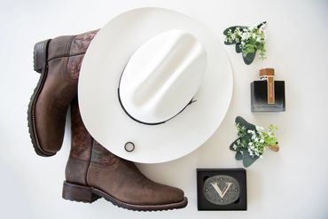 A collection of the grooms accessories for the wedding with a cowboy hat and the ring in the center.