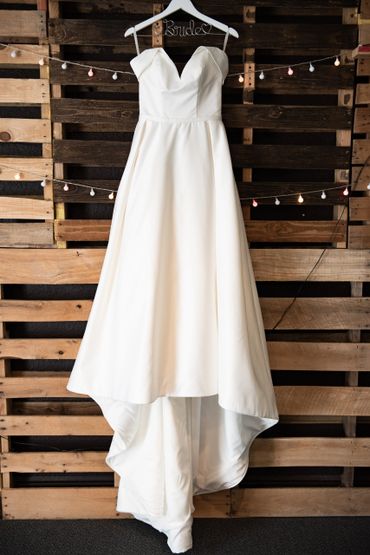 The brides wedding dress drapes in front of a wooden wall laced with twinkling lights.