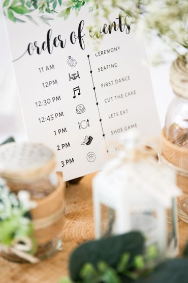 A table card listing the order of events for a wedding is surrounded by green and white flowers. 