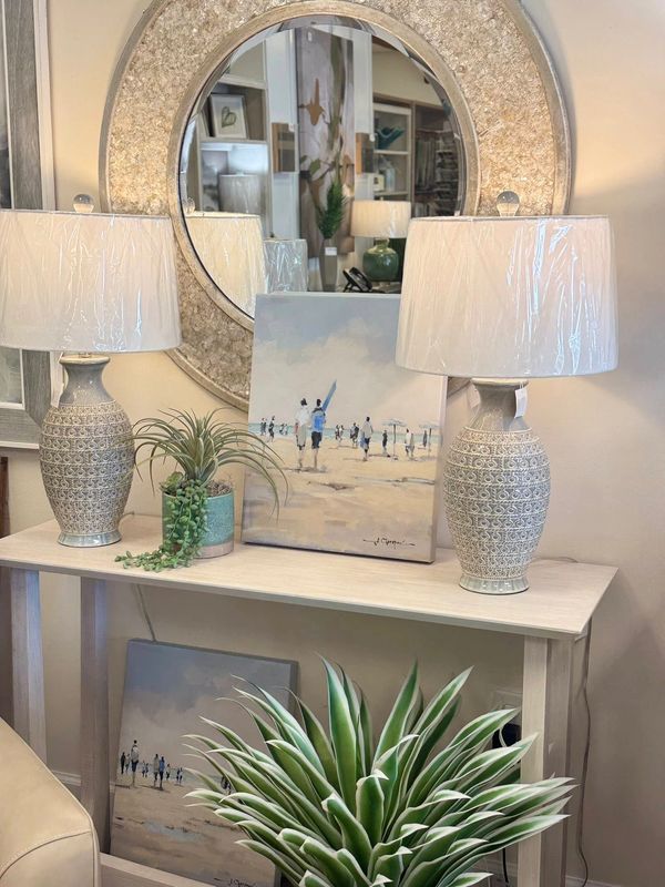Elegant console table with lamps, paintings, and plants under a large round mirror.
