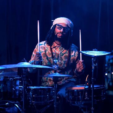 Drummer playing on a drum set under blue stage lighting.