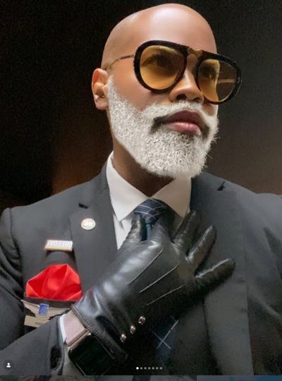 Stylish man with white beard, large sunglasses, and leather gloves.
