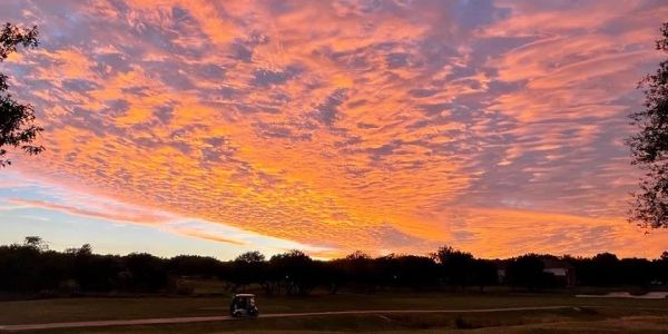 Vibrant sunset sky over a golf course with a cart path and trees.