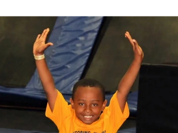 Young boy raising arms, smiling indoors.