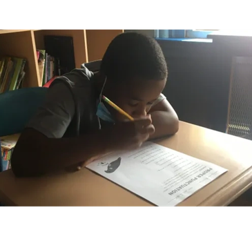 A student focused on writing at a desk in a classroom.