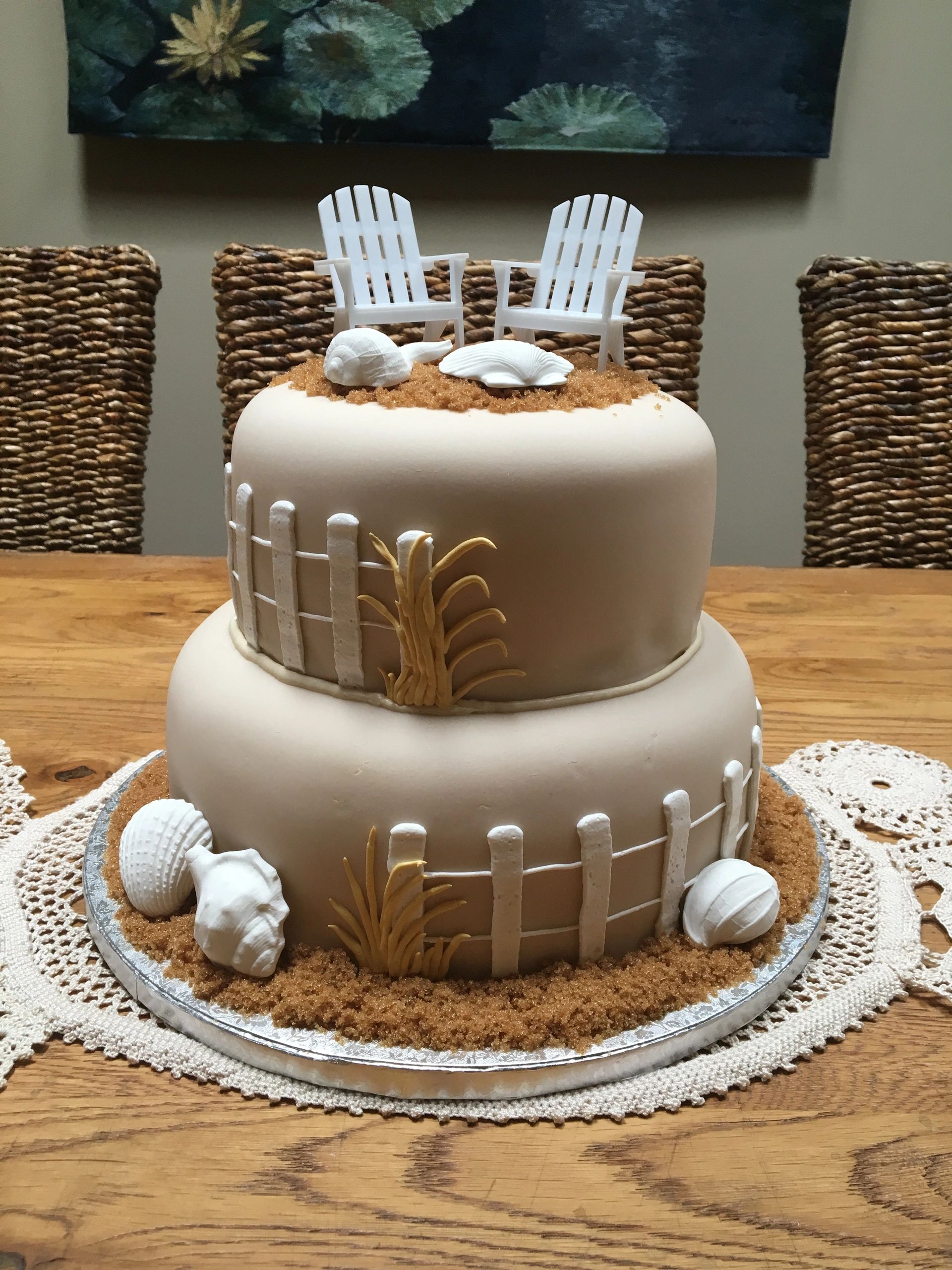 Two-tier beach-themed cake with chairs and seashells.