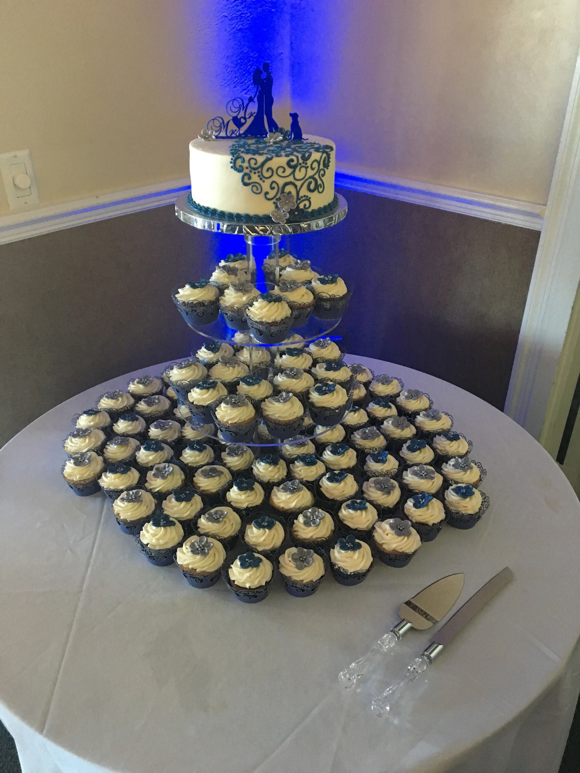 Wedding cake and cupcakes decorated with blue and silver flowers.