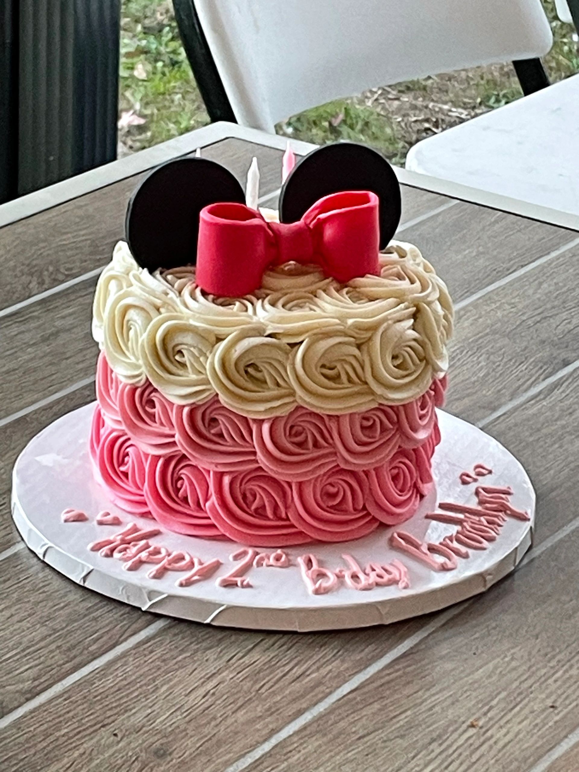 Birthday cake decorated like Minnie Mouse with pink and cream rosettes.