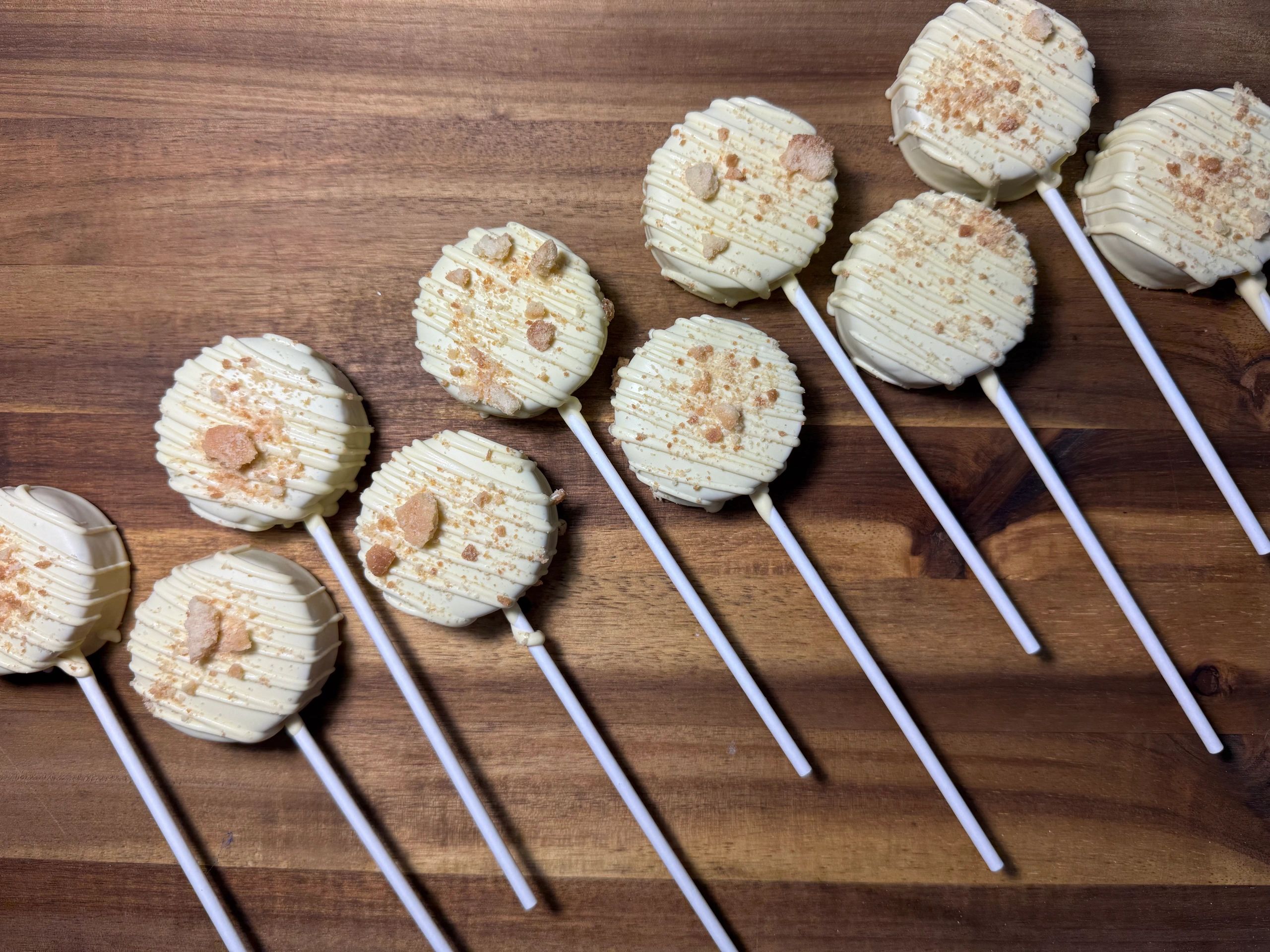 White chocolate-covered pops with crumb topping on a wooden surface.